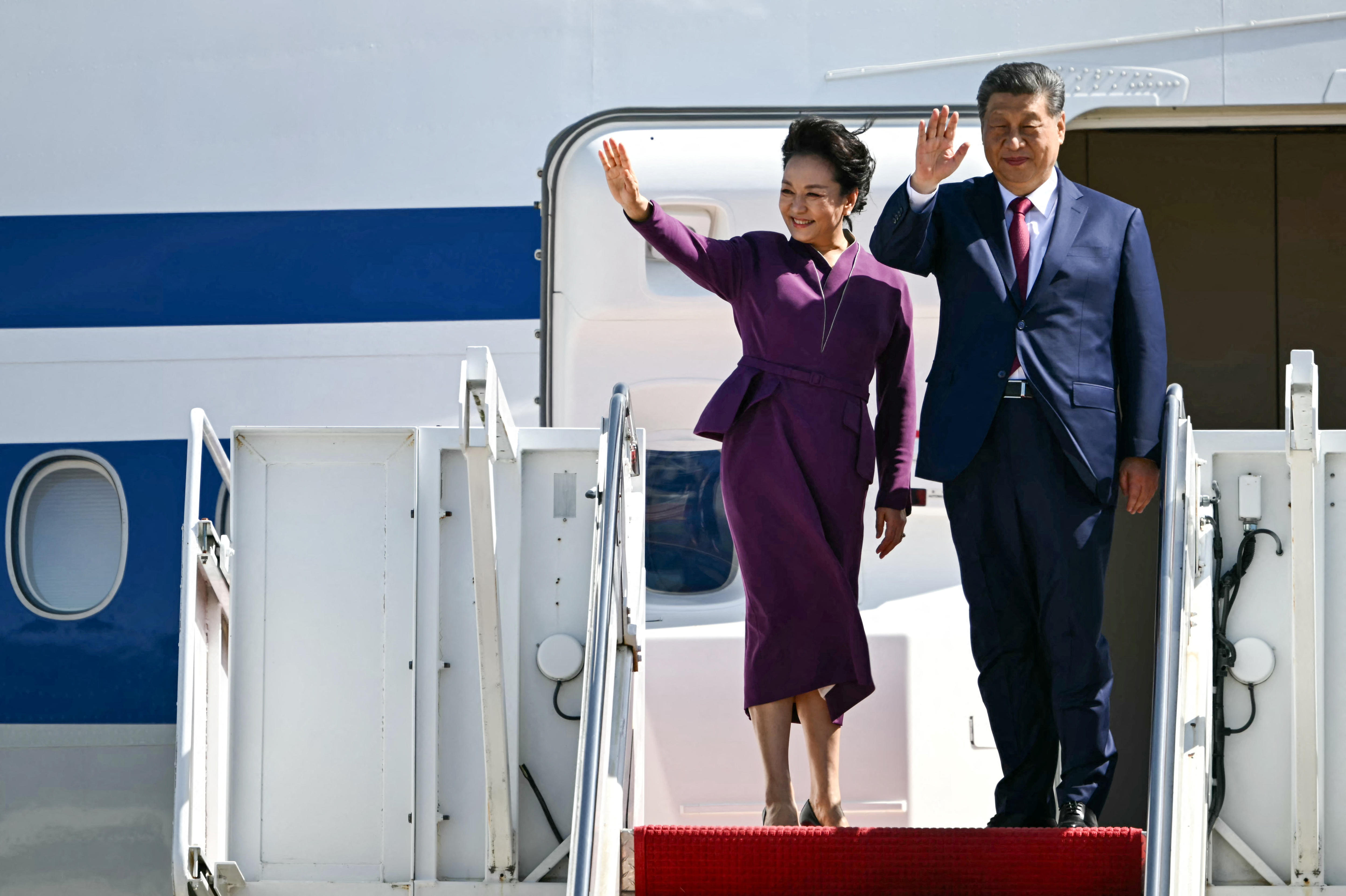 Xi Jinping and wife Peng Liyuan wave at the top of a staircase leading to a plane.