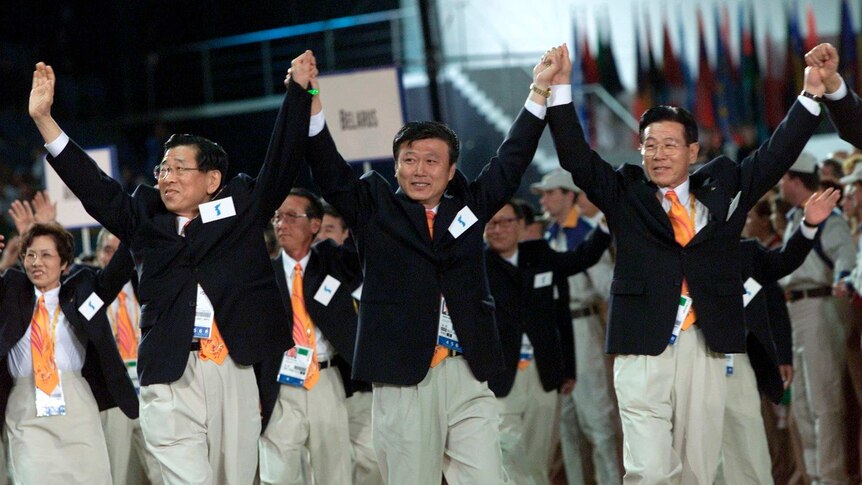 Three men from North and South Korea raise held hands at Sydney Olympic Games opening ceremony