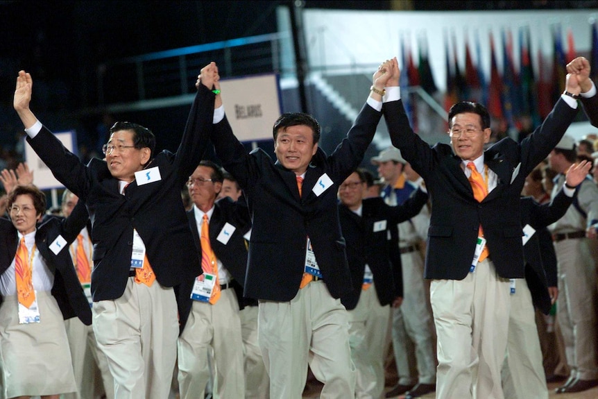 Three men from North and South Korea raise held hands at Sydney Olympic Games opening ceremony