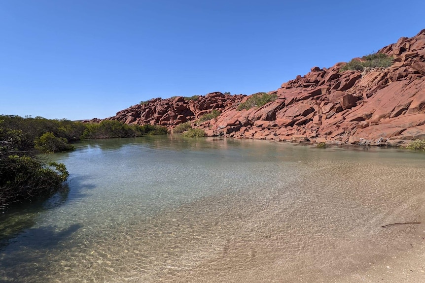 A rocky hill next to a beach with clear blue water.