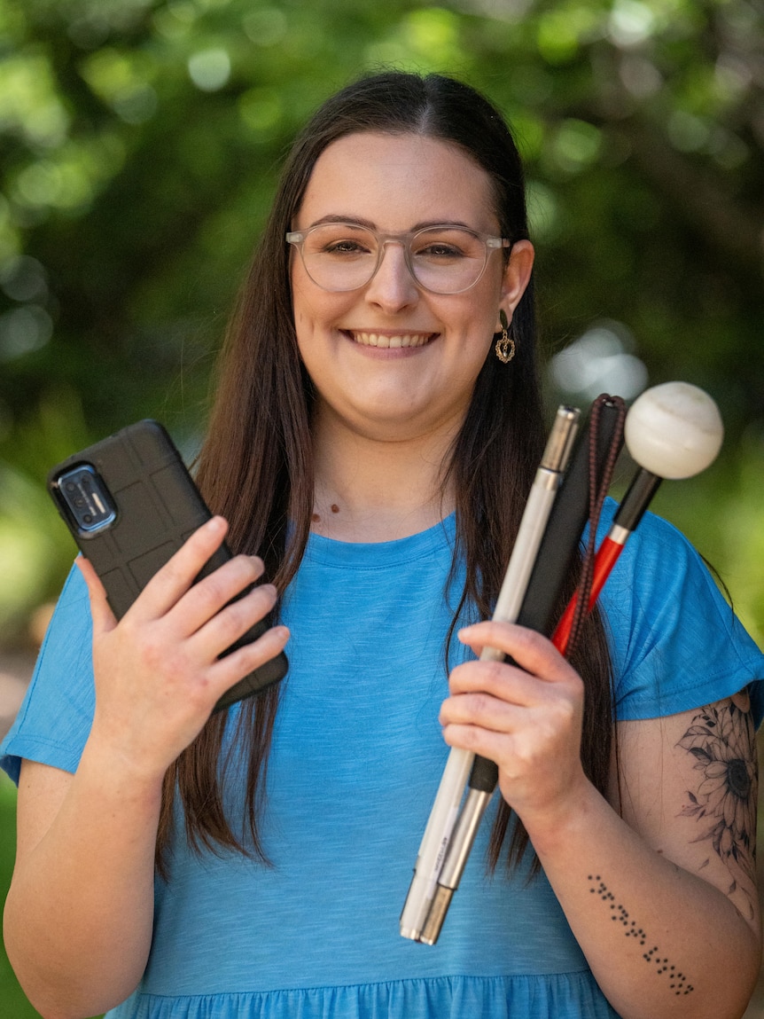 A woman stands with a phone in one hand and three mobility canes in the other