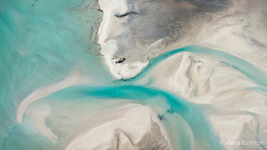 An overheard shot of a beach, with what appears to be a woman's face in the sand