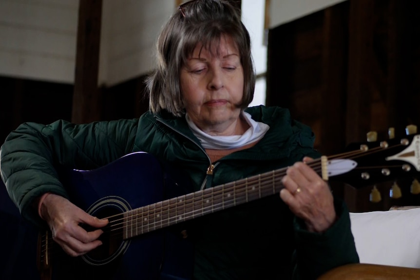 A woman with short hair playing a guitar inside a house