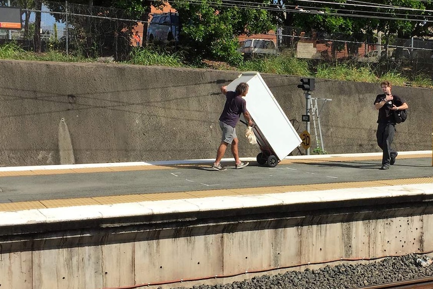 Man pushes a fridge on a trolley along the platform at Bown Hills train station.