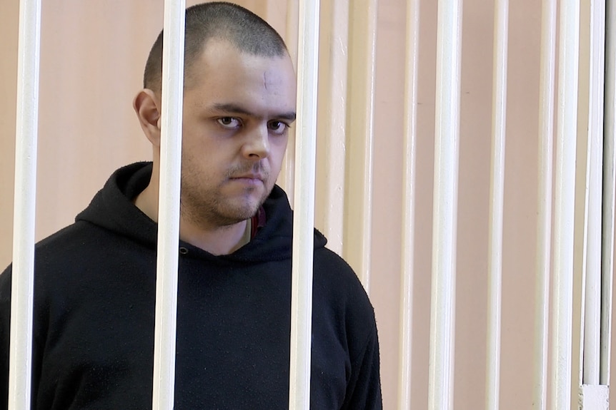 A dishevelled-looking young man is seen behind bars in a jail cell.