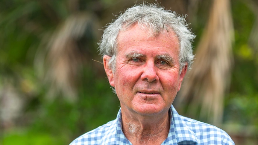 A portrait of Ian Hutton, conservationist, standing in front of a leafy background.