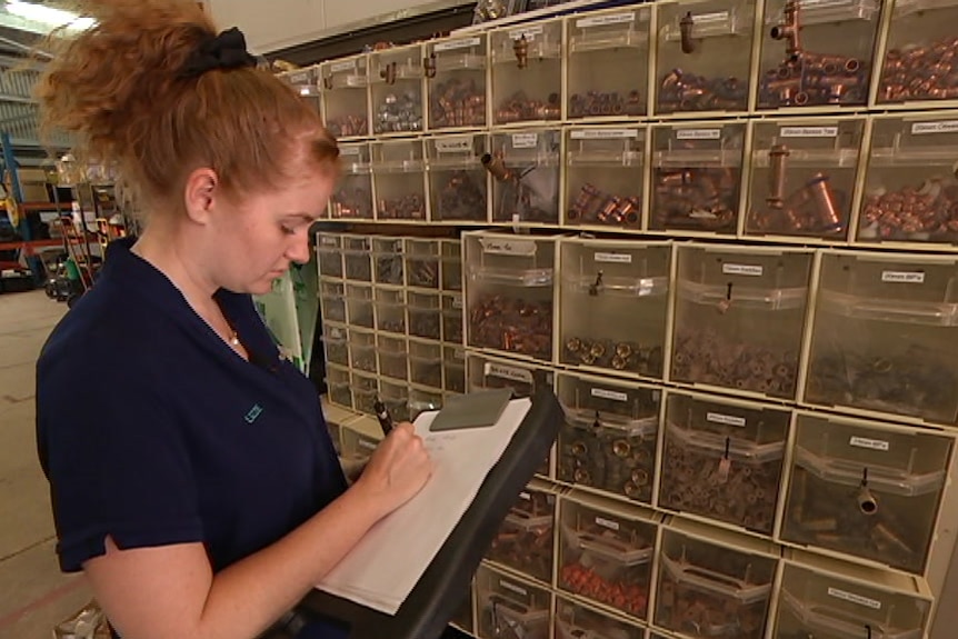 A woman writing notes on a notepad in front of a wall of plumbing parts.