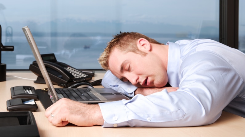 A man lying over his desk at work.