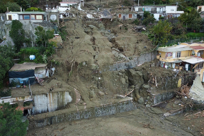 An aerial photo of homes on a hillside, where a landslide has ripped through multiple buildings. 