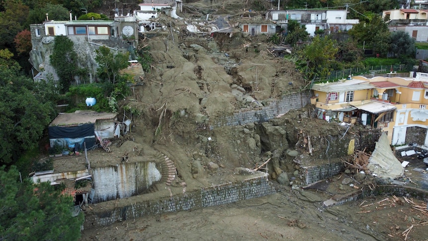 An aerial photo of homes on a hillside, where a landslide has ripped through multiple buildings. 