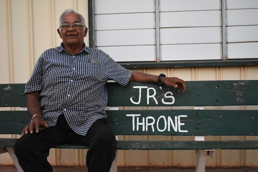 A man sitting on a bench with 'JR's Throne' written on it.