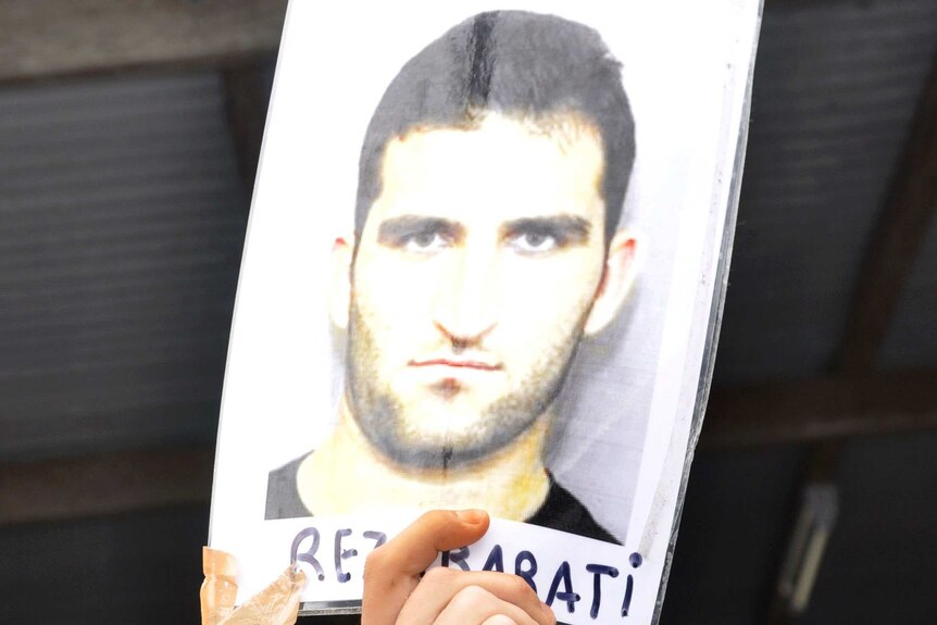 An asylum seeker in Delta compound holds aloft a picture of slain asylum seeker Reza Berati.