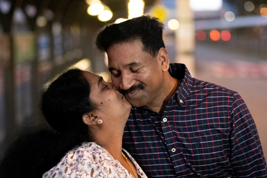 A woman kisses a man on the cheek.