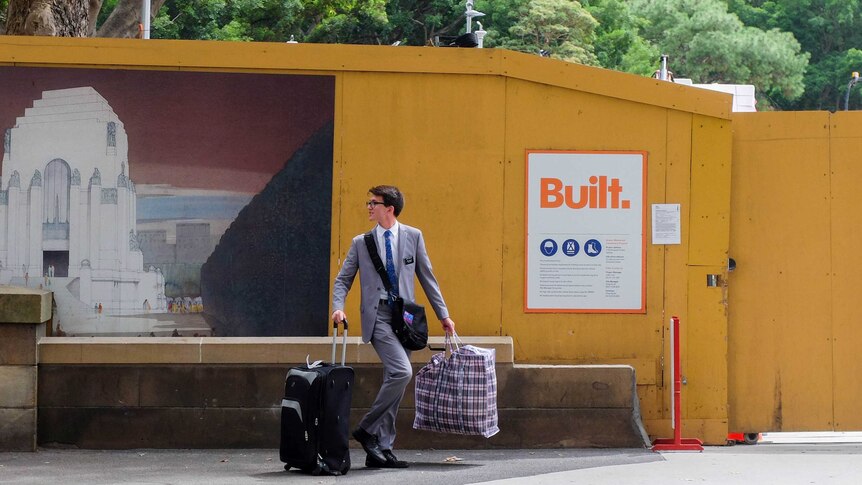 Mormon missionary in suit holding suitcase and bag.