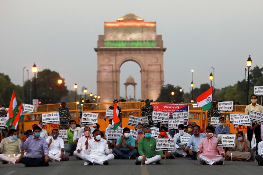 A group of people sit on the ground holding signs and waving flags in front of an arch.