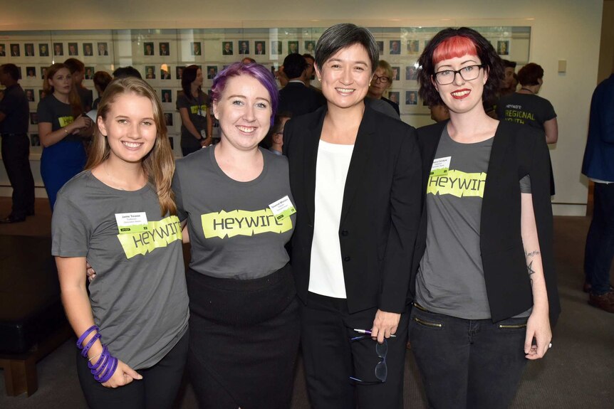 Penny Wong posing for photograph with three young women wearing Heywire t-shirts.