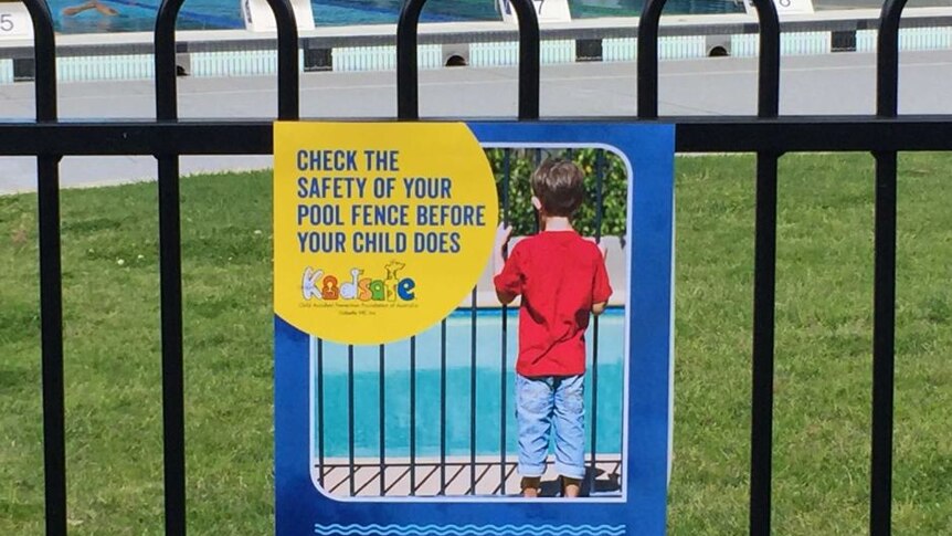 a pool safety sign on a fence. pool in the background