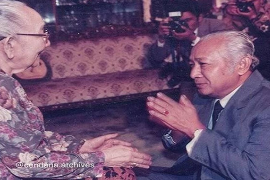 A black and white photo of Indonesia's second president Suharto bowing down and holding his father in law's hands.