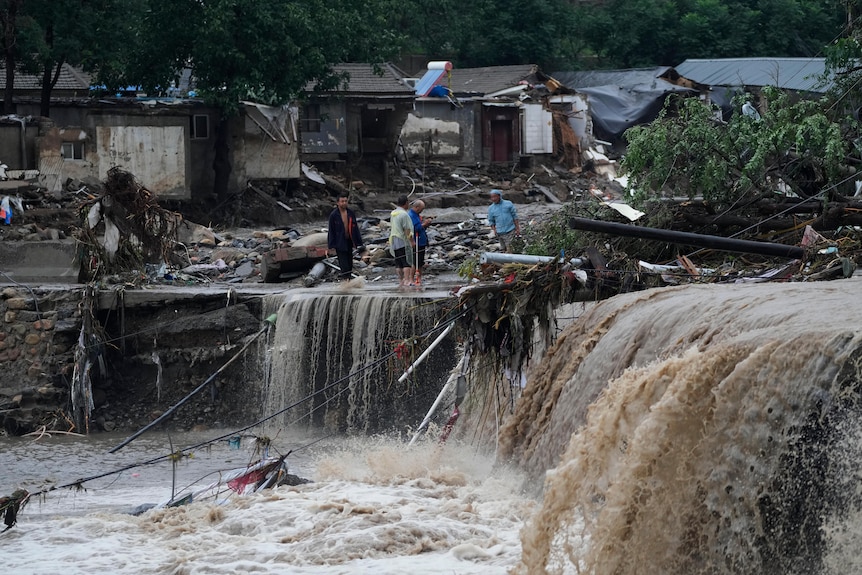Villagers gather near a village damaged by floodwaters.