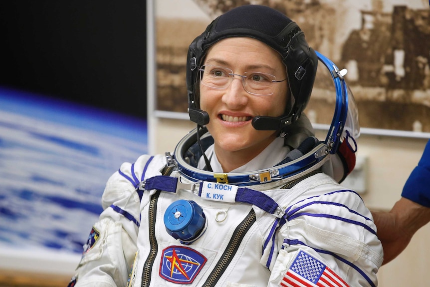 Christina Koch smiles while wearing her spacesuit, sans the helmet.