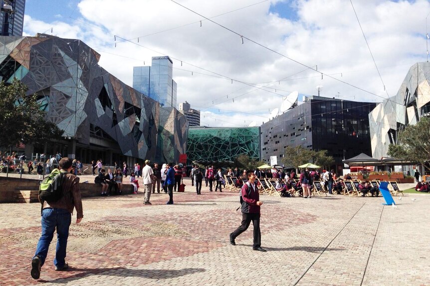 People walking around and sitting in Federation Square on a sunny day.