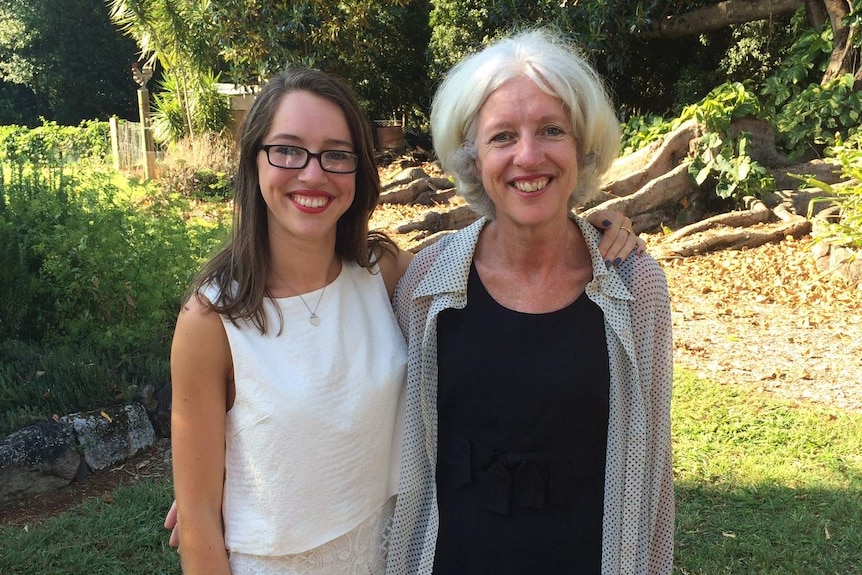 Isabelle Burke and Christine O'Brien stand embracing in a garden