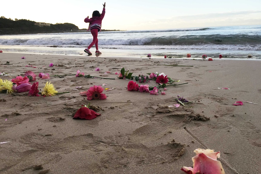 A young girl throws flowers into the water. More flowers are on the sand.