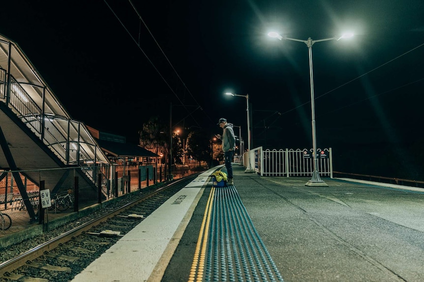 Louis Giles on his phone on a train platform at Woy Woy station waiting for a train.