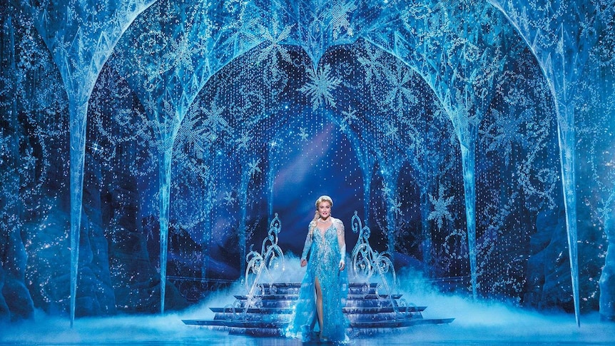 Jemma Rix playing Elsa in Frozen alone on stage wearing a blue sparkly dress against an icy blue backdrop.