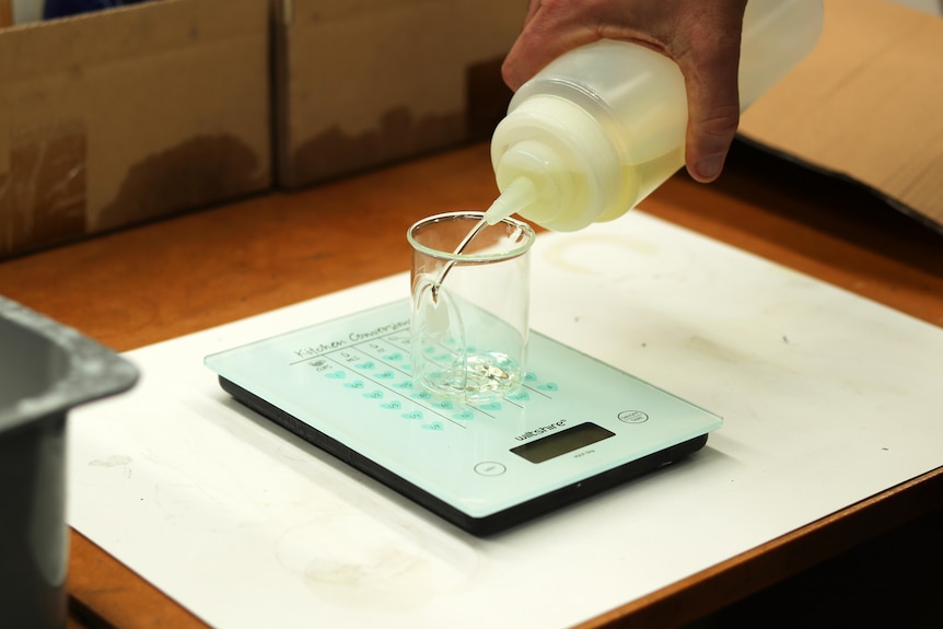 Liquid is poured from a bottle into a beaker sitting on a set of scales.
