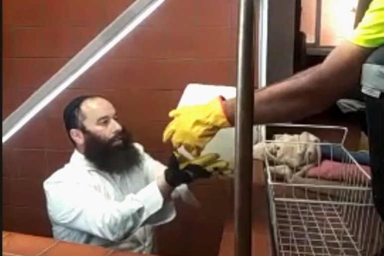Photograph of two men loading blocks of ice, one man is wearing gloves and the other a jewish skullcap and with a long beard