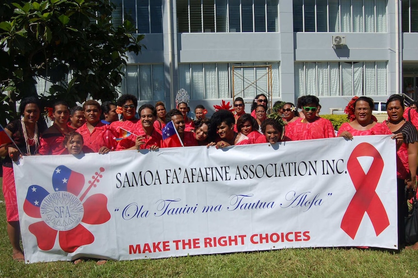 A group of people from the Samoa Fa'afafine Association wearing red with a banner against AIDS.