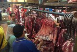 Three people standing at a market stall in Indoneisa, with meat hanging from hooks.