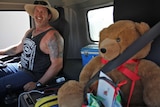 Truck driver Allan Hughes sits next to a stuffed teddy bear in the cabin of a truck.