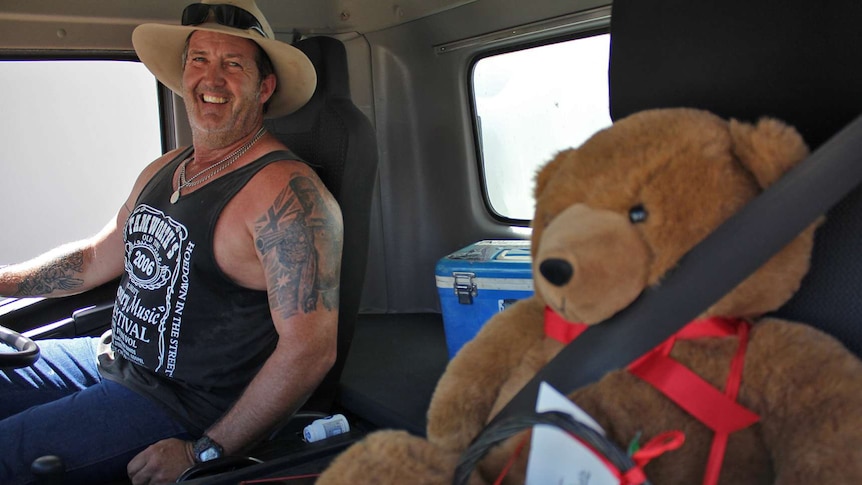 Truck driver Allan Hughes sits next to a stuffed teddy bear in the cabin of a truck.