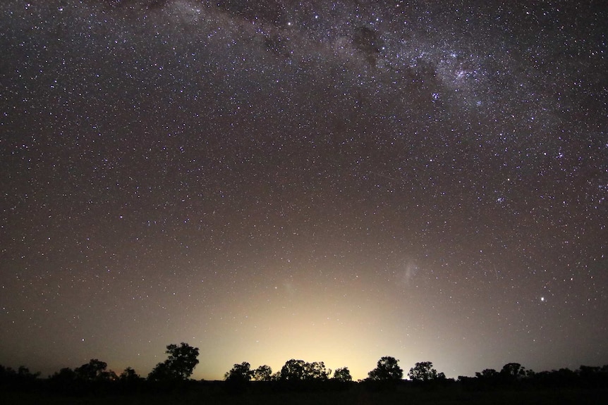 A night sky filled with stars, with a large glow rising above the landscape below.