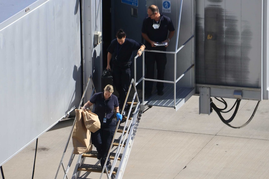 Police in navy uniforms walk down some stairs next to a plain carrying brown paper bags.