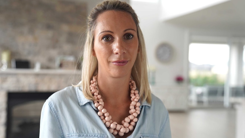 Michelle in her living room, wearing a chambray shirt and necklace made of pale pink beads.
