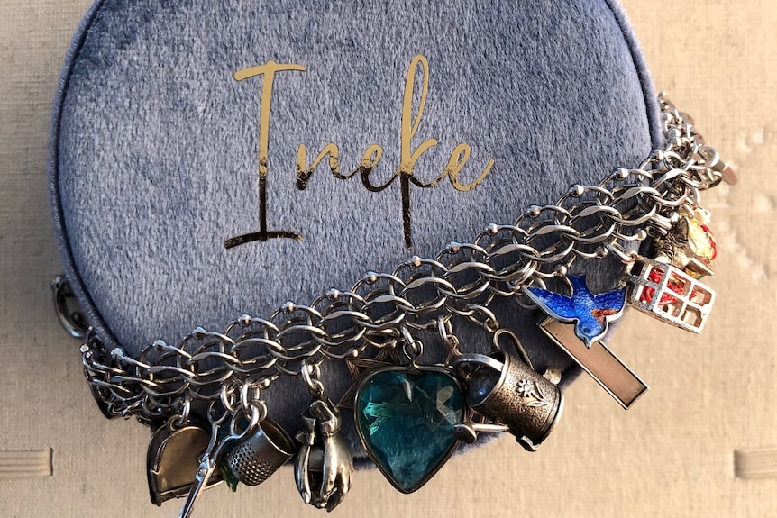 Close-up of a silver charm bracelet with many coloured charms attached, wrapped around a velvet blue box with 'Ineke' on it.