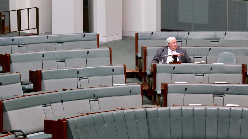 Wide view of Clive Palmer sitting in an empty House of Representatives Chamber.