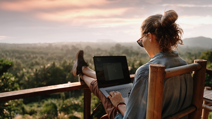 Woman sits on the balcony with her laptop.