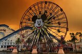 An orange sky with dark smoke is seen over the rollercoasters and Mickey Mouse ferris wheel at Disneyland.