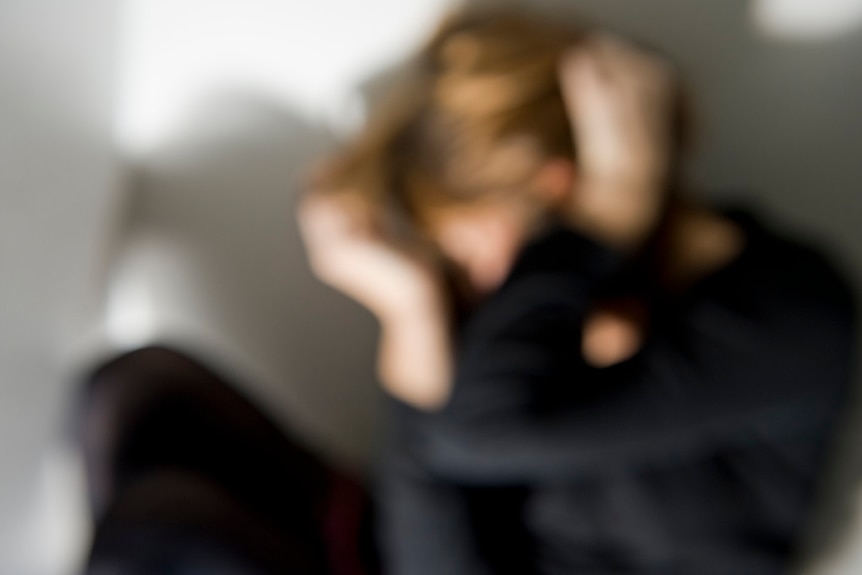 A blurred figure in dark clothing covers their face.