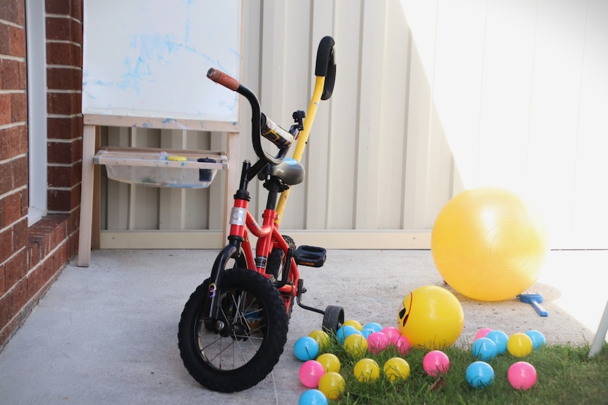 A children's tricycle sits on the pavement surrounded by ball pit balls.