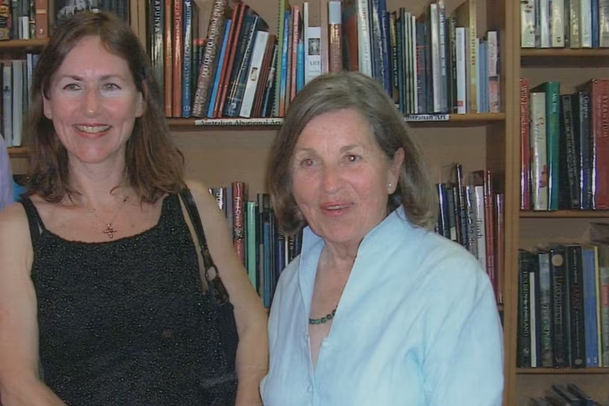 Two women pose for a photo in front of a bookcase