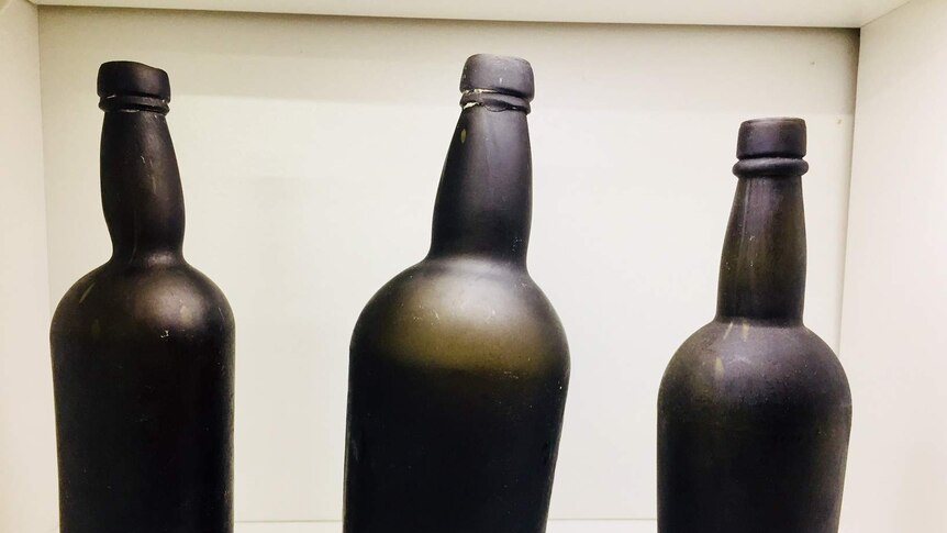Three wonky handmade black bottles from the 1800s on a white table