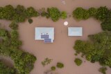 Top down view of a house flooded, only the roof can be seen, surrounded by brown water