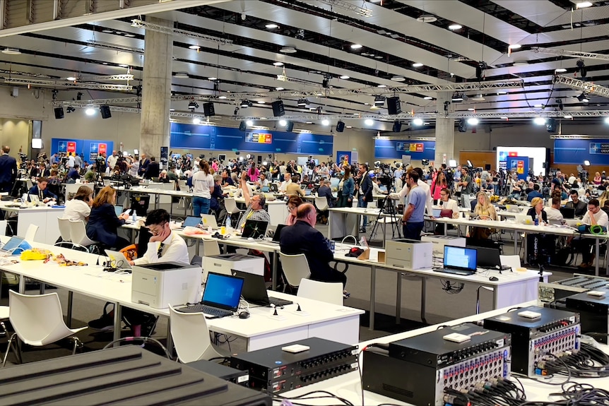 Journalists work at desks inside a large media centre.