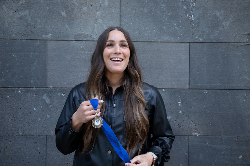 Courtney stands in front of a brick wall with a medal and smiles.