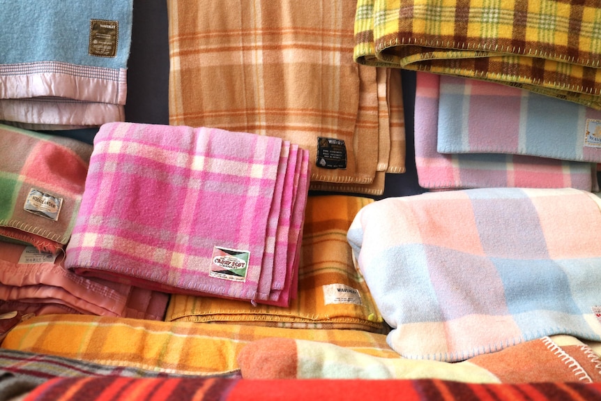 a collection of old woollen blankets in shades of pink, blue and orange